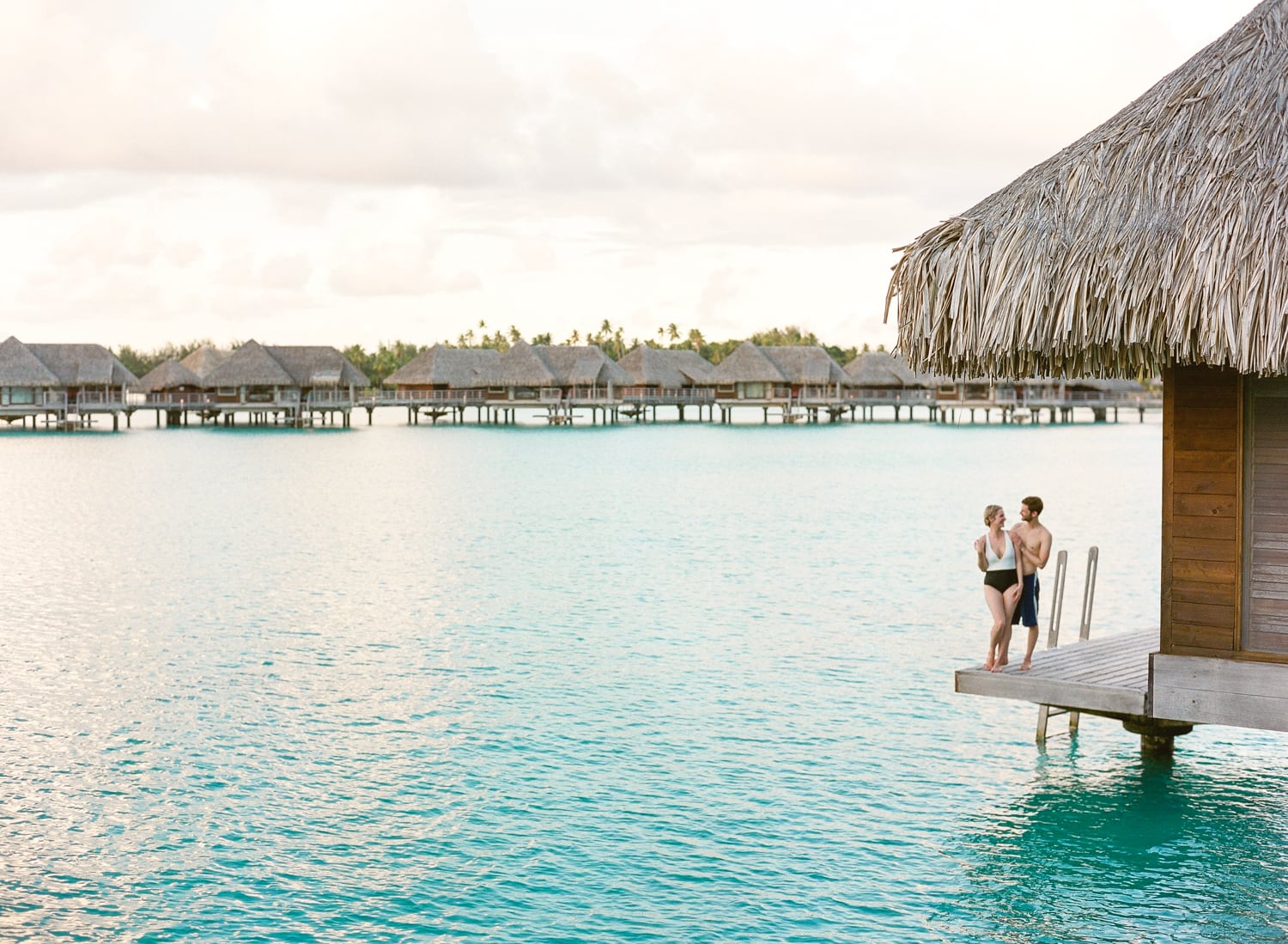 A couple on honeymoon on the desk of their overwater bungalow at the Intercontinental Bora Bora, scenic view with the landscape and blue water
